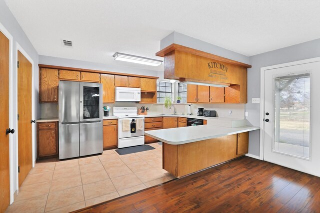 kitchen with light wood-type flooring, white appliances, kitchen peninsula, and a wealth of natural light