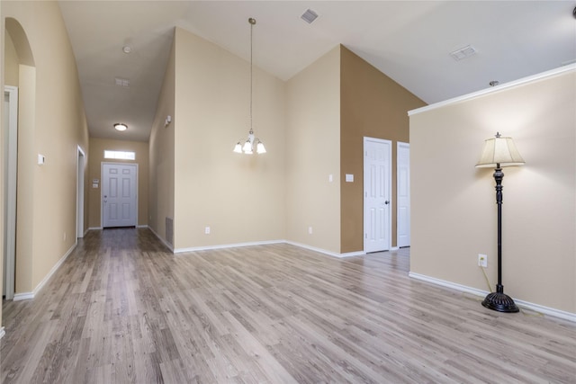 unfurnished room with an inviting chandelier, high vaulted ceiling, and light hardwood / wood-style floors