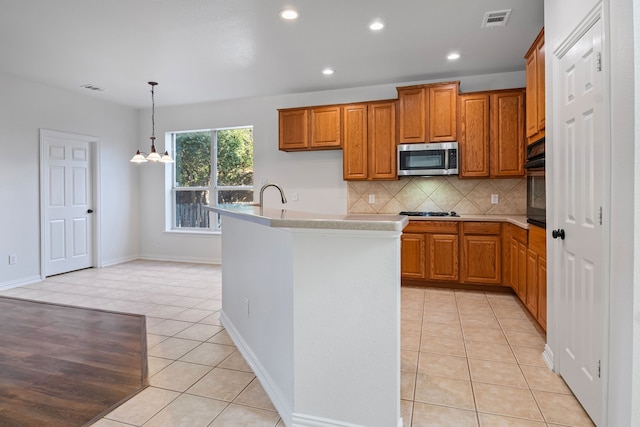 kitchen with decorative backsplash, appliances with stainless steel finishes, a kitchen island with sink, light tile patterned floors, and a chandelier