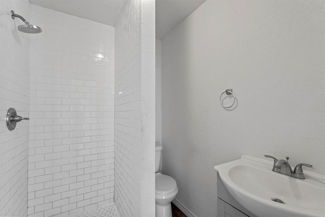 bathroom with tiled shower, vanity, and toilet