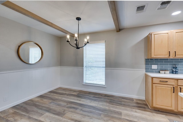 unfurnished dining area featuring a chandelier, beam ceiling, and light wood-type flooring