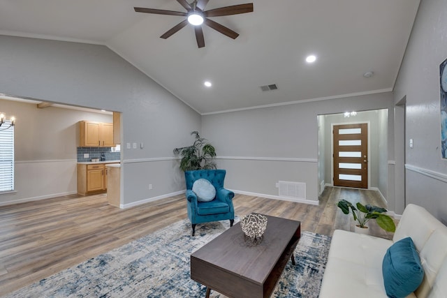 living room with ceiling fan with notable chandelier, light hardwood / wood-style floors, ornamental molding, and vaulted ceiling