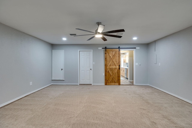 unfurnished room featuring a barn door, ceiling fan, and light colored carpet