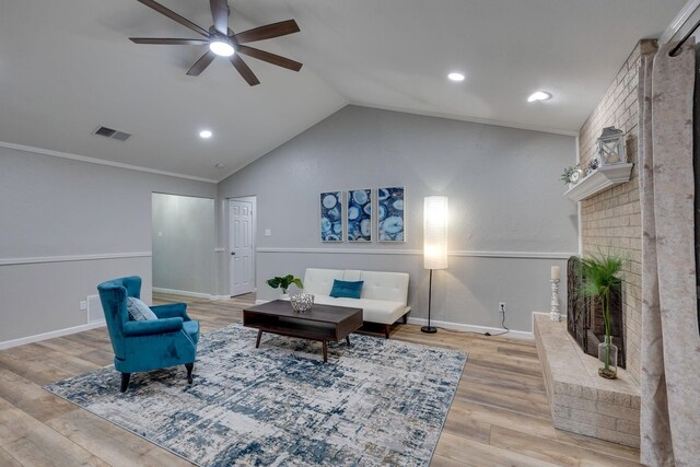 living area with a brick fireplace, vaulted ceiling, ceiling fan, ornamental molding, and light hardwood / wood-style floors