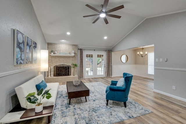 living room with lofted ceiling, french doors, ceiling fan with notable chandelier, hardwood / wood-style flooring, and a fireplace