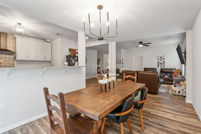 dining room with ceiling fan with notable chandelier and light hardwood / wood-style floors