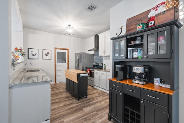 kitchen with sink, wall chimney range hood, appliances with stainless steel finishes, white cabinetry, and wood counters