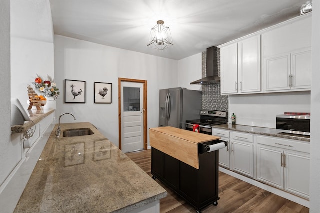 kitchen featuring sink, decorative light fixtures, appliances with stainless steel finishes, wall chimney range hood, and white cabinets