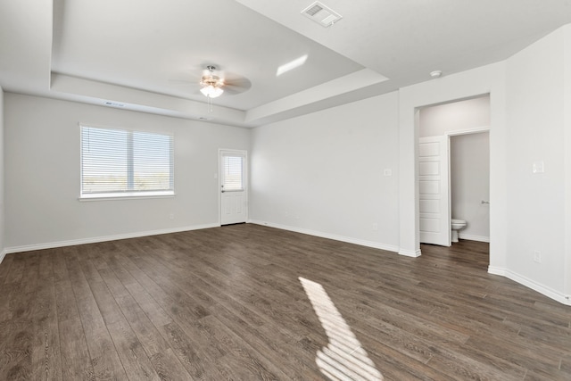 empty room featuring a tray ceiling, ceiling fan, and dark wood-type flooring