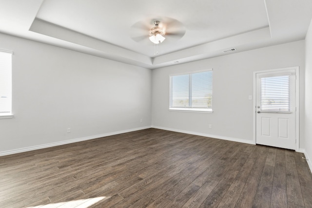 unfurnished room featuring a raised ceiling, a healthy amount of sunlight, and dark hardwood / wood-style floors