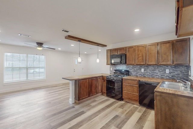 kitchen featuring kitchen peninsula, light wood-type flooring, sink, black appliances, and pendant lighting