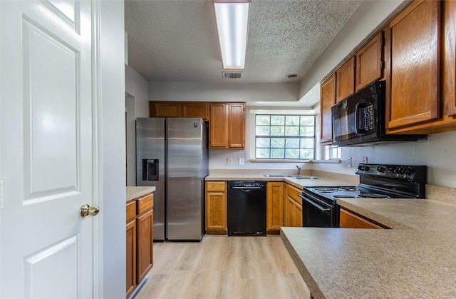 kitchen with sink, black appliances, a textured ceiling, and light hardwood / wood-style floors