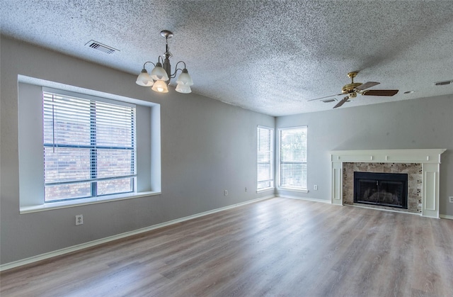 unfurnished living room featuring ceiling fan with notable chandelier, a textured ceiling, light wood-type flooring, and a tiled fireplace