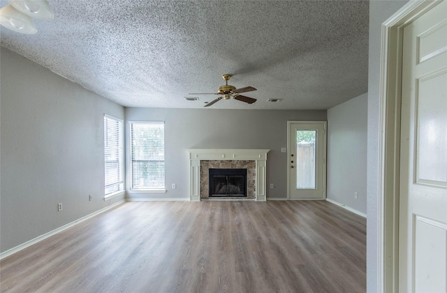 unfurnished living room with a tiled fireplace, ceiling fan, a textured ceiling, and light wood-type flooring