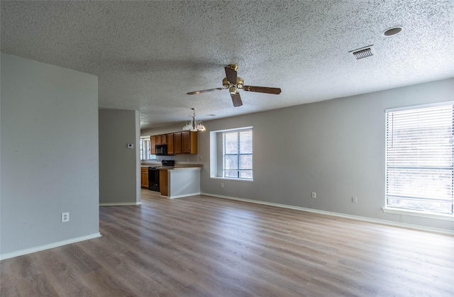 unfurnished living room with ceiling fan with notable chandelier, a textured ceiling, and light hardwood / wood-style flooring