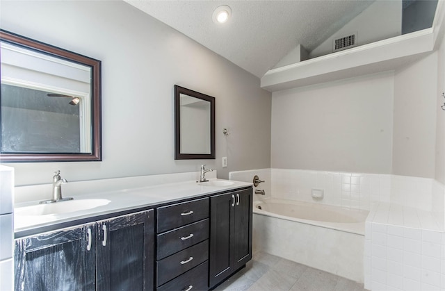 bathroom with a bathtub, vanity, a textured ceiling, vaulted ceiling, and tile patterned flooring