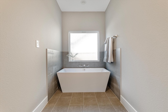 bathroom with a tub to relax in, tile patterned flooring, and tile walls