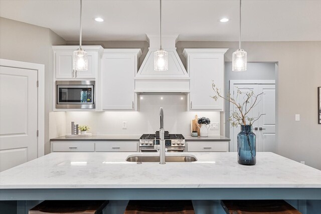 kitchen with appliances with stainless steel finishes, decorative light fixtures, custom exhaust hood, and an island with sink