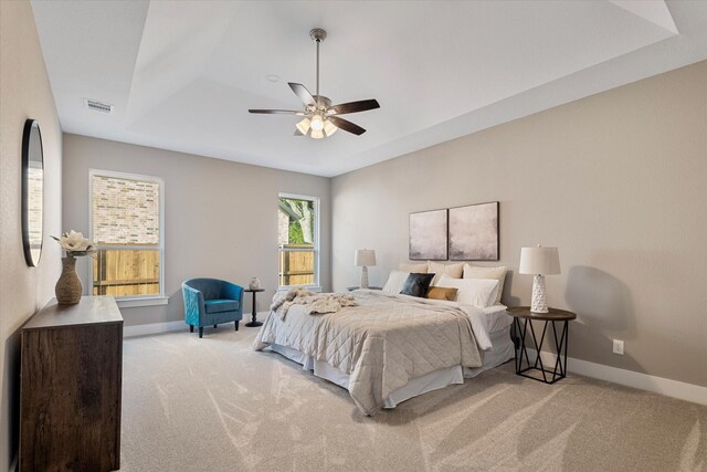 bedroom featuring light carpet, a tray ceiling, and ceiling fan