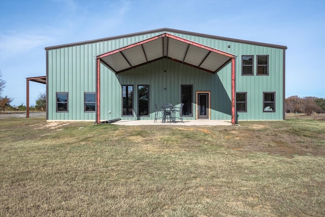 back of property featuring board and batten siding, a detached garage, a patio, and a lawn