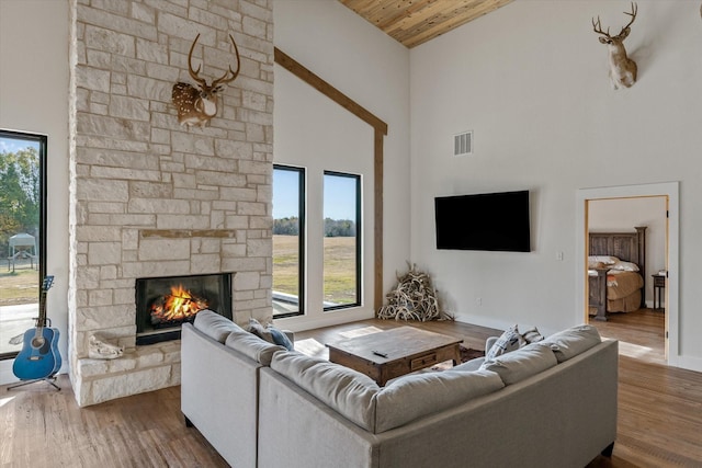 living area featuring high vaulted ceiling, a fireplace, visible vents, and wood finished floors