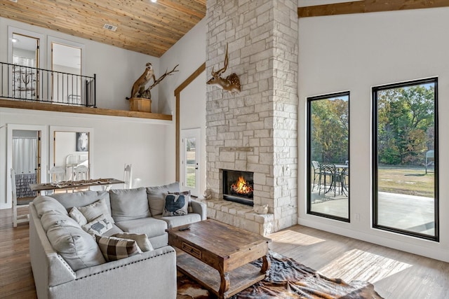 living room with high vaulted ceiling, wood ceiling, a stone fireplace, and wood finished floors