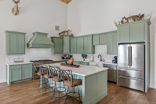 kitchen with premium appliances, a kitchen island, light countertops, premium range hood, and green cabinetry