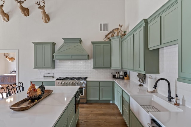 kitchen with high end stainless steel range, visible vents, green cabinets, a sink, and premium range hood