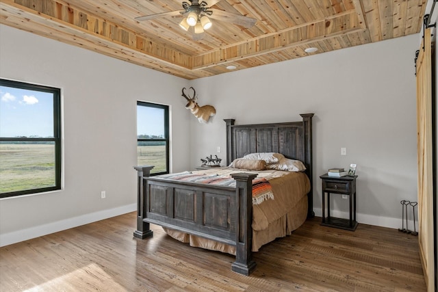 bedroom with a barn door, baseboards, wooden ceiling, ceiling fan, and wood finished floors