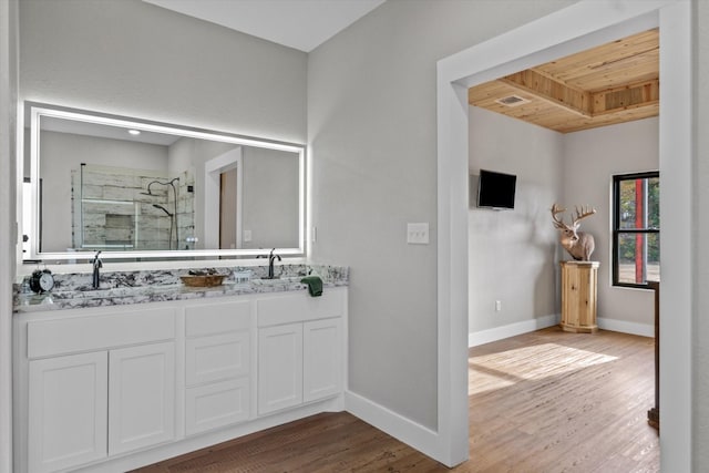 bathroom featuring double vanity, baseboards, wood finished floors, a shower stall, and a sink