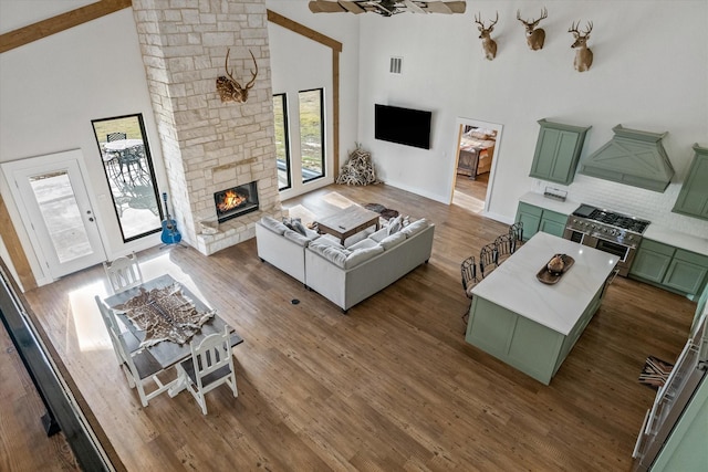 living room featuring high vaulted ceiling, a stone fireplace, wood finished floors, and visible vents