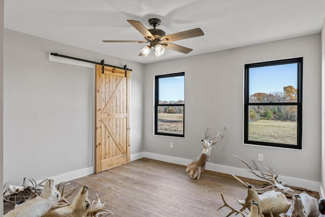 interior space with a barn door, baseboards, ceiling fan, and wood finished floors