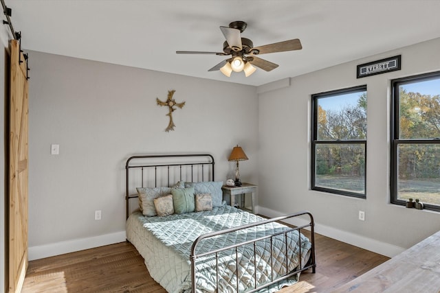 bedroom featuring a barn door, baseboards, ceiling fan, and wood finished floors