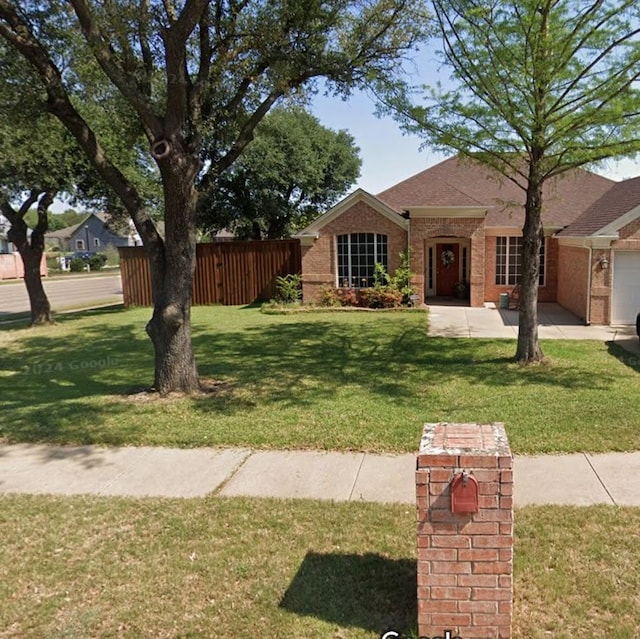 view of front facade with brick siding, a front lawn, a shingled roof, and fence