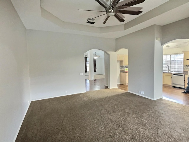 carpeted empty room with baseboards, arched walkways, a raised ceiling, ceiling fan, and a sink