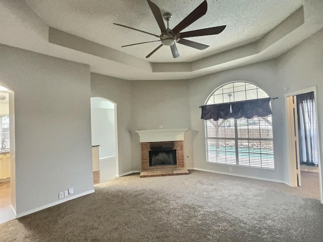 unfurnished living room featuring ceiling fan, a fireplace, carpet flooring, baseboards, and a raised ceiling