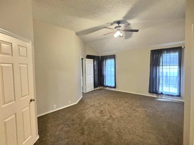 unfurnished bedroom featuring dark carpet, a ceiling fan, vaulted ceiling, a textured ceiling, and baseboards