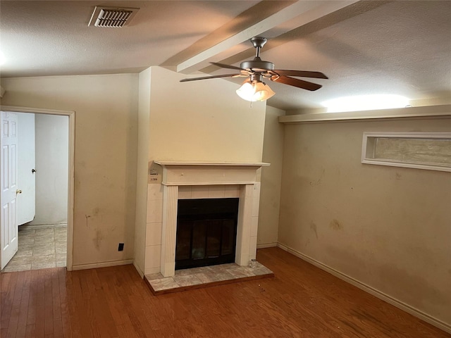 unfurnished living room featuring vaulted ceiling with beams, visible vents, a ceiling fan, wood finished floors, and a tile fireplace