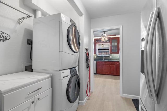 washroom with sink, ceiling fan, stacked washing maching and dryer, cabinets, and light hardwood / wood-style floors