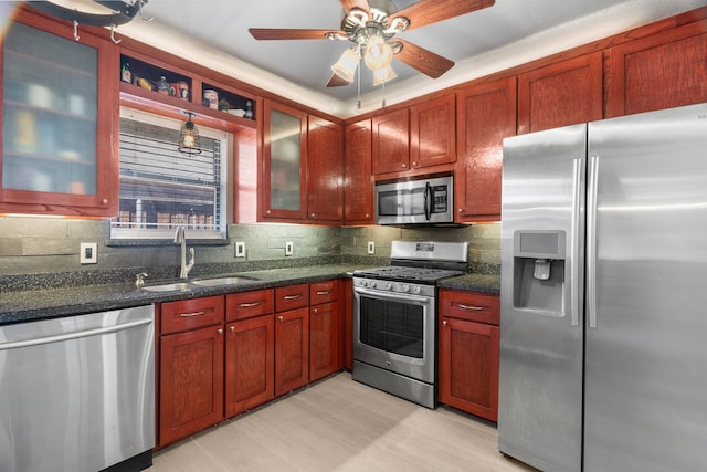 kitchen with sink, ceiling fan, dark stone countertops, stainless steel appliances, and tasteful backsplash