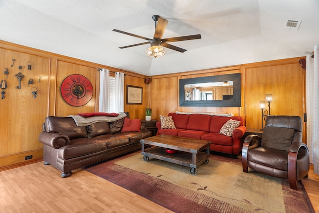 living room featuring vaulted ceiling, wood walls, ceiling fan, and light wood-type flooring