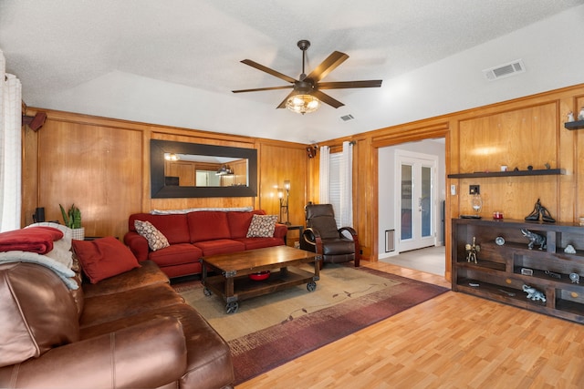 living room with wood walls, vaulted ceiling, a textured ceiling, ceiling fan, and hardwood / wood-style floors