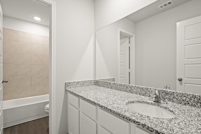 full bathroom featuring hardwood / wood-style flooring, vanity, tiled shower / bath, and toilet