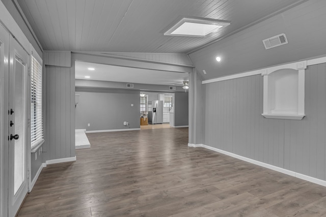 unfurnished living room featuring lofted ceiling with skylight, wooden walls, ceiling fan, and wood-type flooring