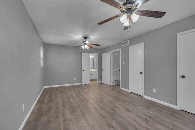 unfurnished bedroom featuring connected bathroom, two closets, light hardwood / wood-style flooring, and ceiling fan