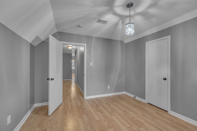 unfurnished bedroom featuring a chandelier, light hardwood / wood-style flooring, and lofted ceiling