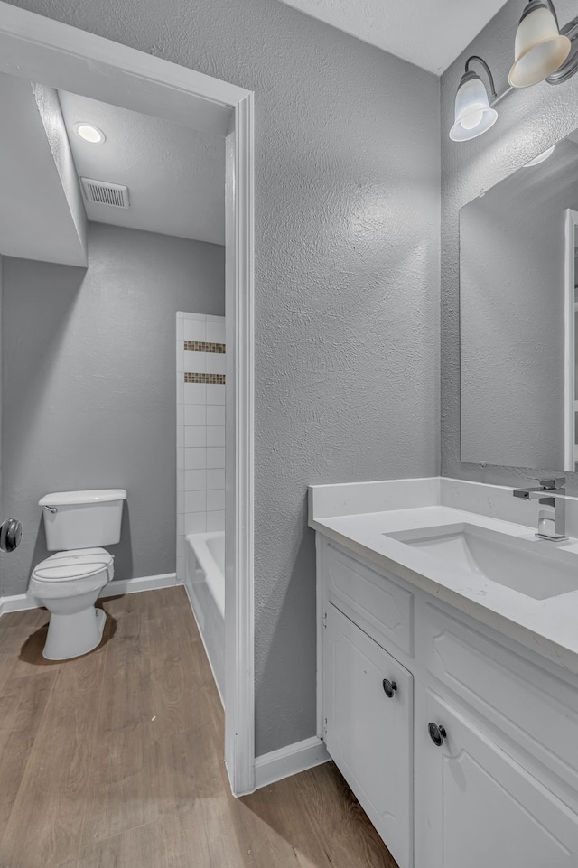 full bathroom featuring hardwood / wood-style floors, vanity, a textured ceiling, shower / washtub combination, and toilet