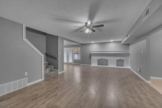 unfurnished living room with ceiling fan, a textured ceiling, a brick fireplace, and light hardwood / wood-style flooring