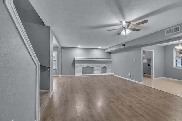 unfurnished living room featuring ceiling fan, a fireplace, wood-type flooring, and a textured ceiling