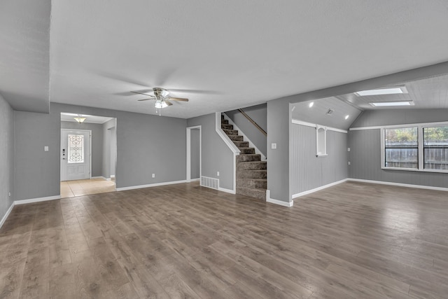 unfurnished living room featuring lofted ceiling with skylight, hardwood / wood-style floors, a textured ceiling, and ceiling fan